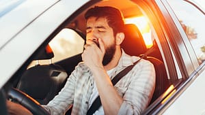 Tired man yawning while driving a white car